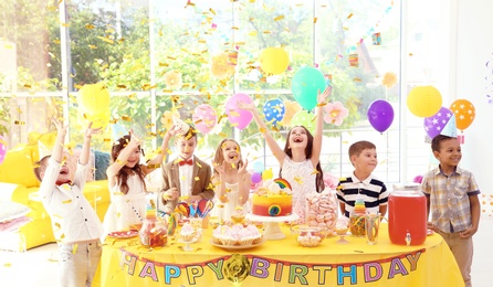 Photo of Cute children near table with treats at birthday party indoors