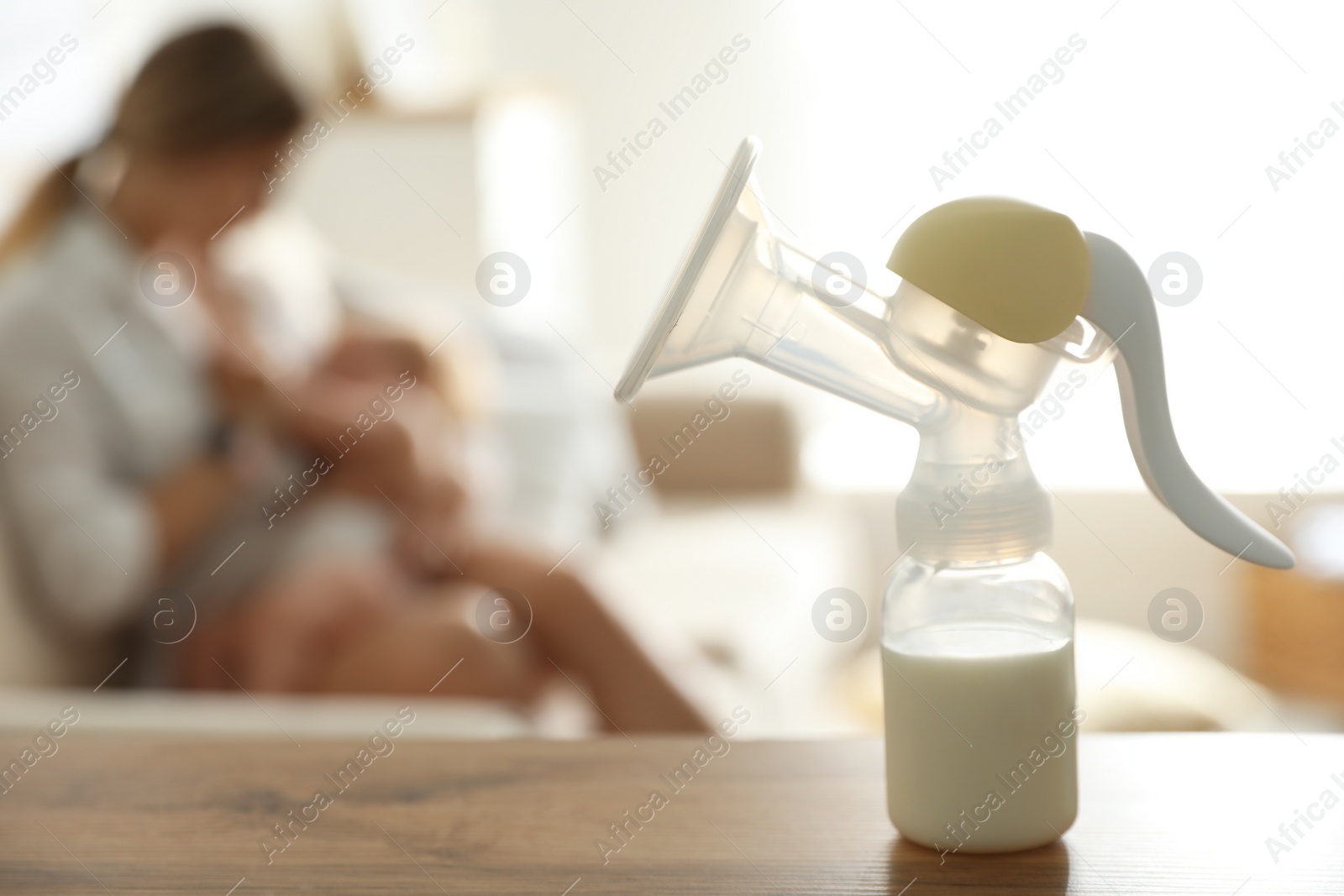 Photo of Mother feeding her little baby at home, focus on breast pump with milk. Healthy growth