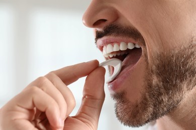 Photo of Man putting chewing gum into mouth on blurred background, closeup