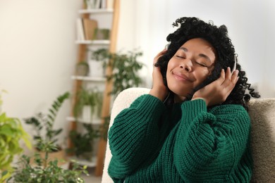 Photo of Relaxing atmosphere. Woman wearing headphones and listening music in room with beautiful houseplants. Space for text