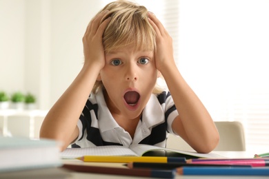 Emotional little boy doing homework at table indoors