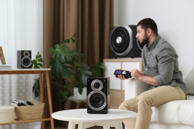 Man using remote to control modern audio speaker system in bright room