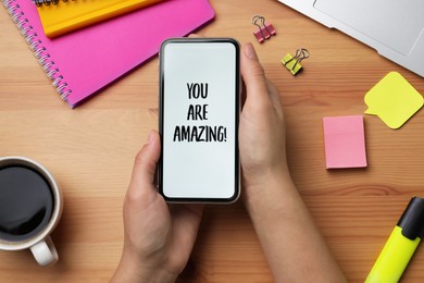 Closeup of woman holding smartphone with phrase You Are Amazing on screen, top view