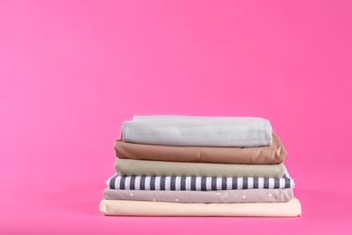 Stack of clean bed sheets on pink background. Space for text