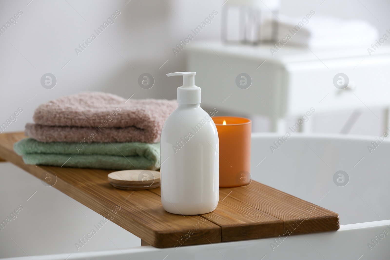 Photo of Tray with bottle of bubble bath, towels and candle on tub in bathroom