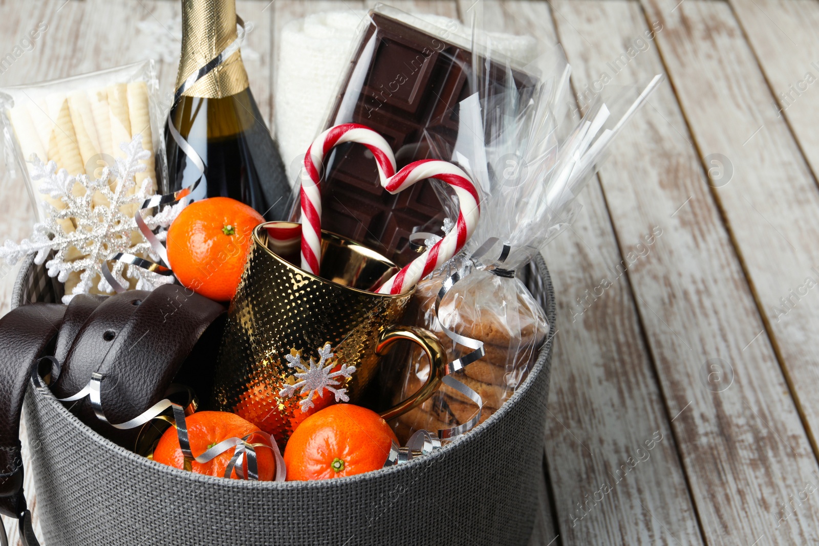 Photo of Christmas gift basket with champagne, candy canes and tangerines on white wooden table, closeup