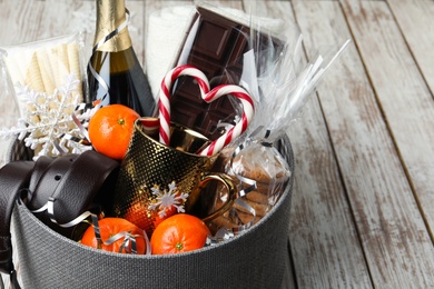 Christmas gift basket with champagne, candy canes and tangerines on white wooden table, closeup