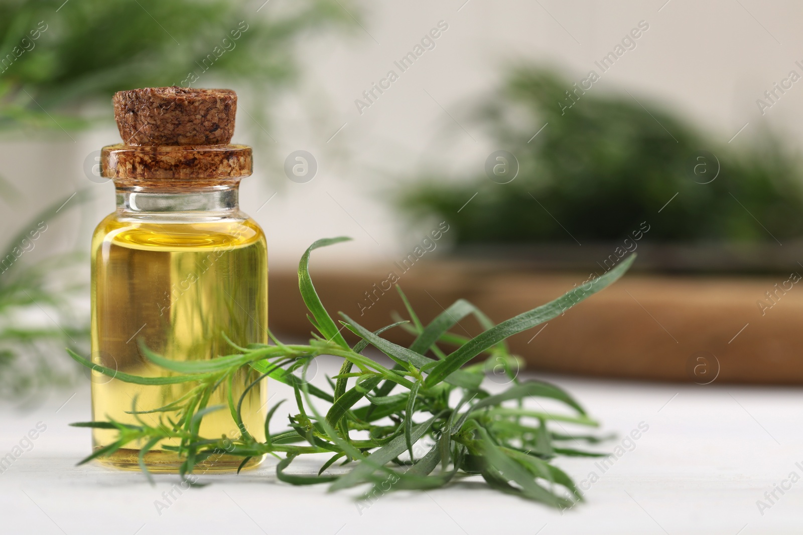 Photo of Bottle of essential oil and fresh tarragon leaves on white wooden table. Space for text