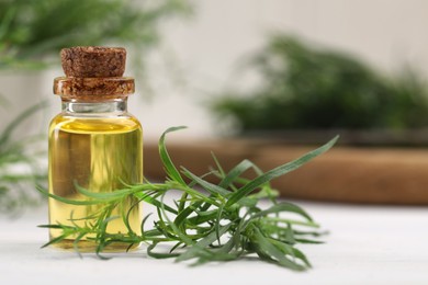 Bottle of essential oil and fresh tarragon leaves on white wooden table. Space for text