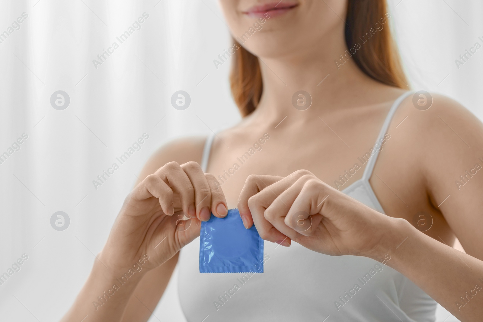 Photo of Woman opening condom indoors, closeup. Safe sex