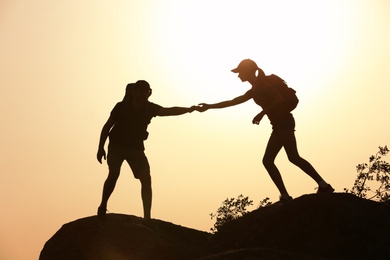 Silhouettes of man and woman helping each other to climb on hill against sunset