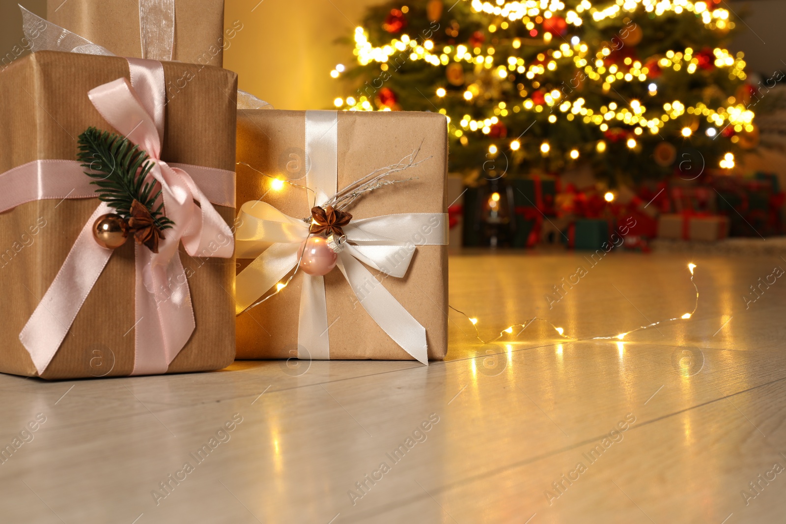 Photo of Beautiful gift boxes against fir tree with Christmas lights indoors, space for text