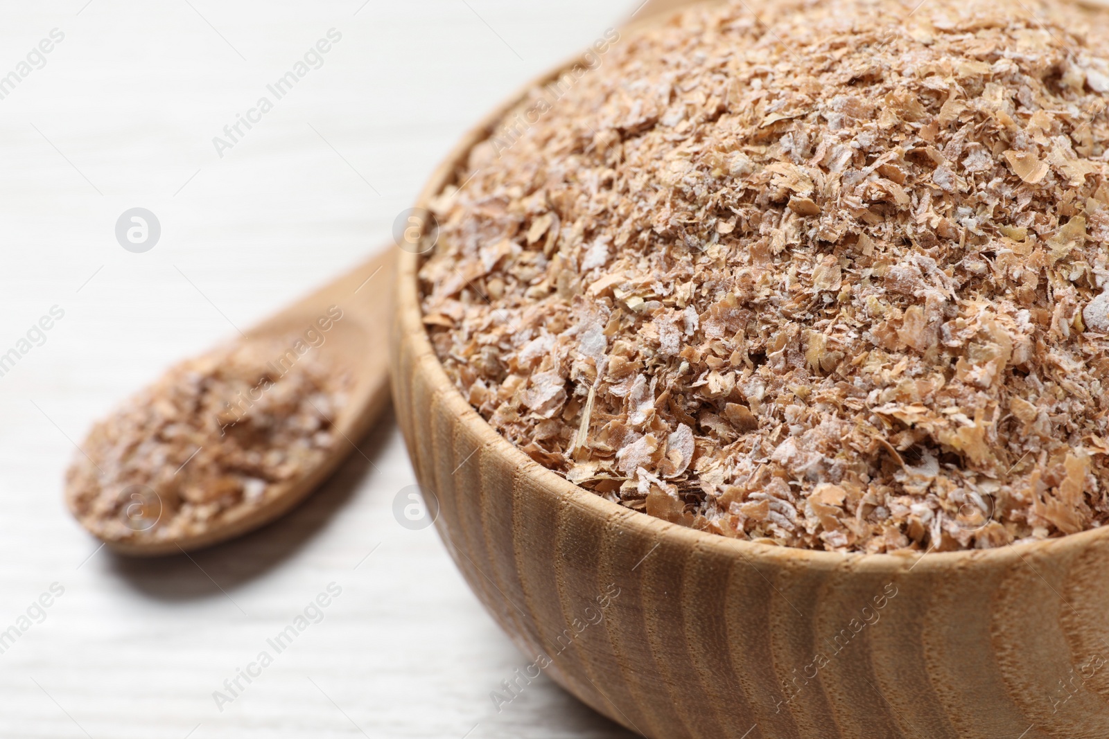 Photo of Bowl of wheat bran on white wooden table, closeup