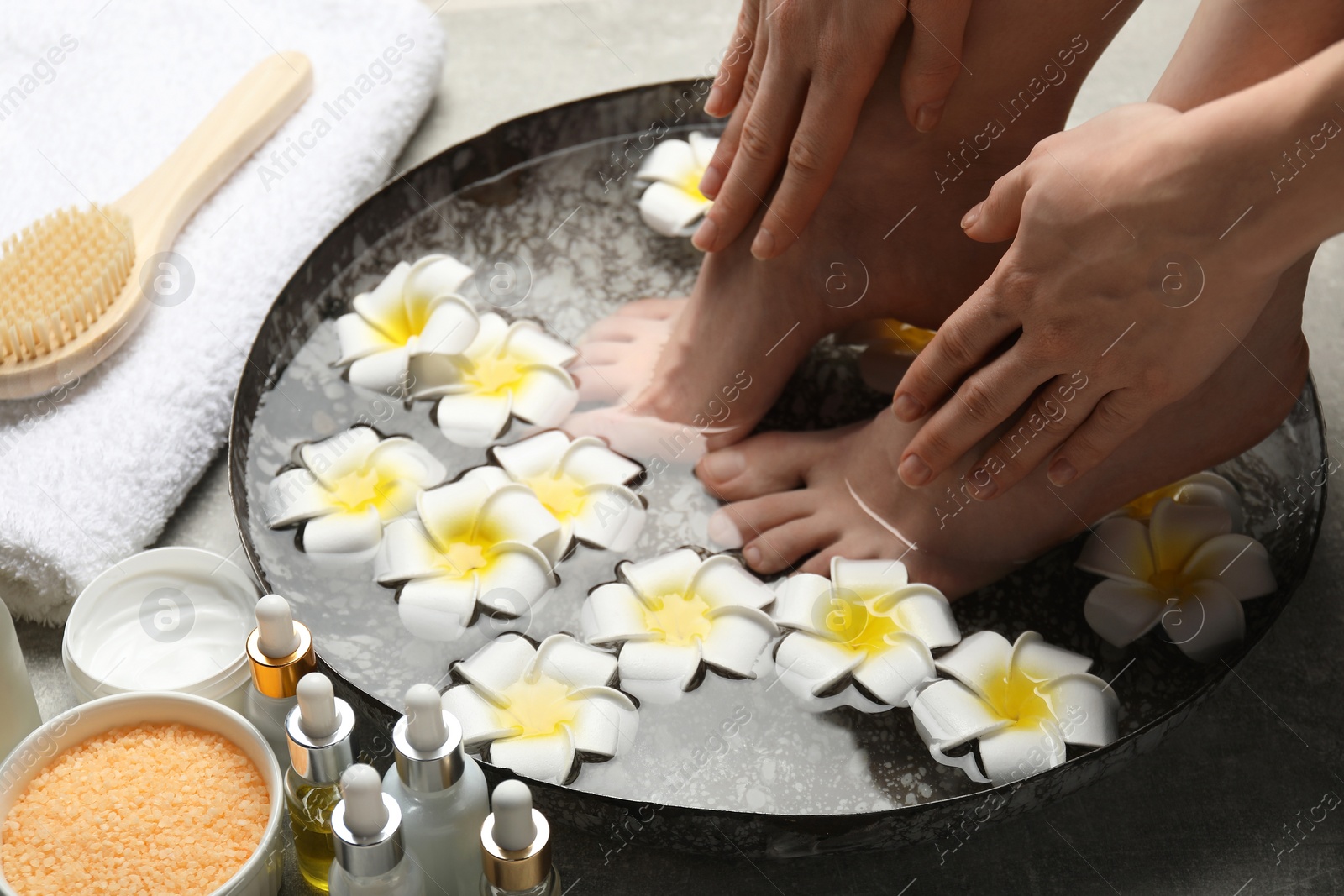 Photo of Woman soaking her feet in bowl with water and flowers on floor, closeup. Spa treatment