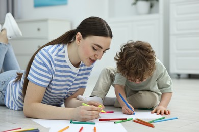 Mother and her little son drawing with colorful markers on floor at home