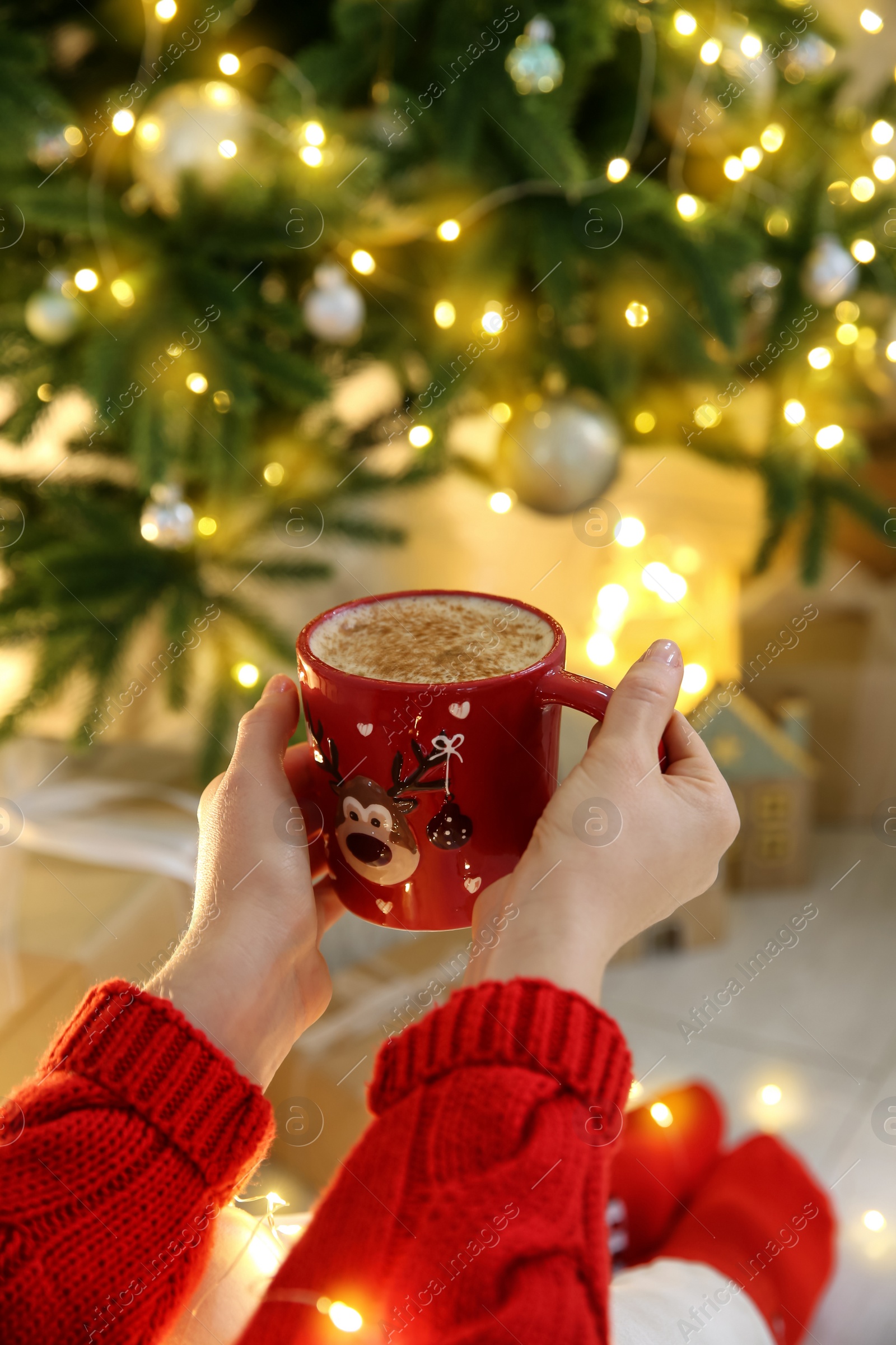 Photo of Woman holding festive cup with coffee near Christmas tree indoors, closeup