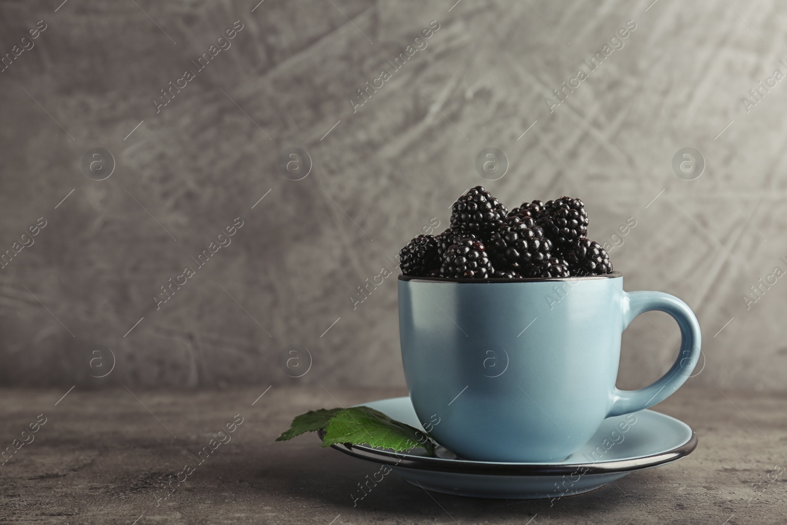 Photo of Mug with fresh blackberry on gray table. Space for text