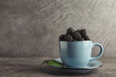 Photo of Mug with fresh blackberry on gray table. Space for text