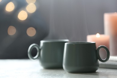 Cups of hot drink on white table against blurred background, space for text