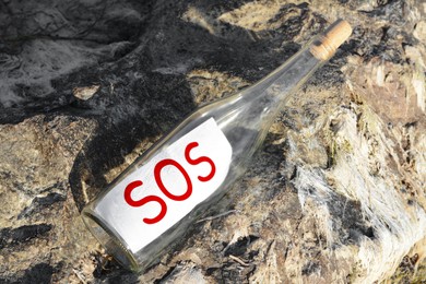 Glass bottle with SOS message on sea rock, top view