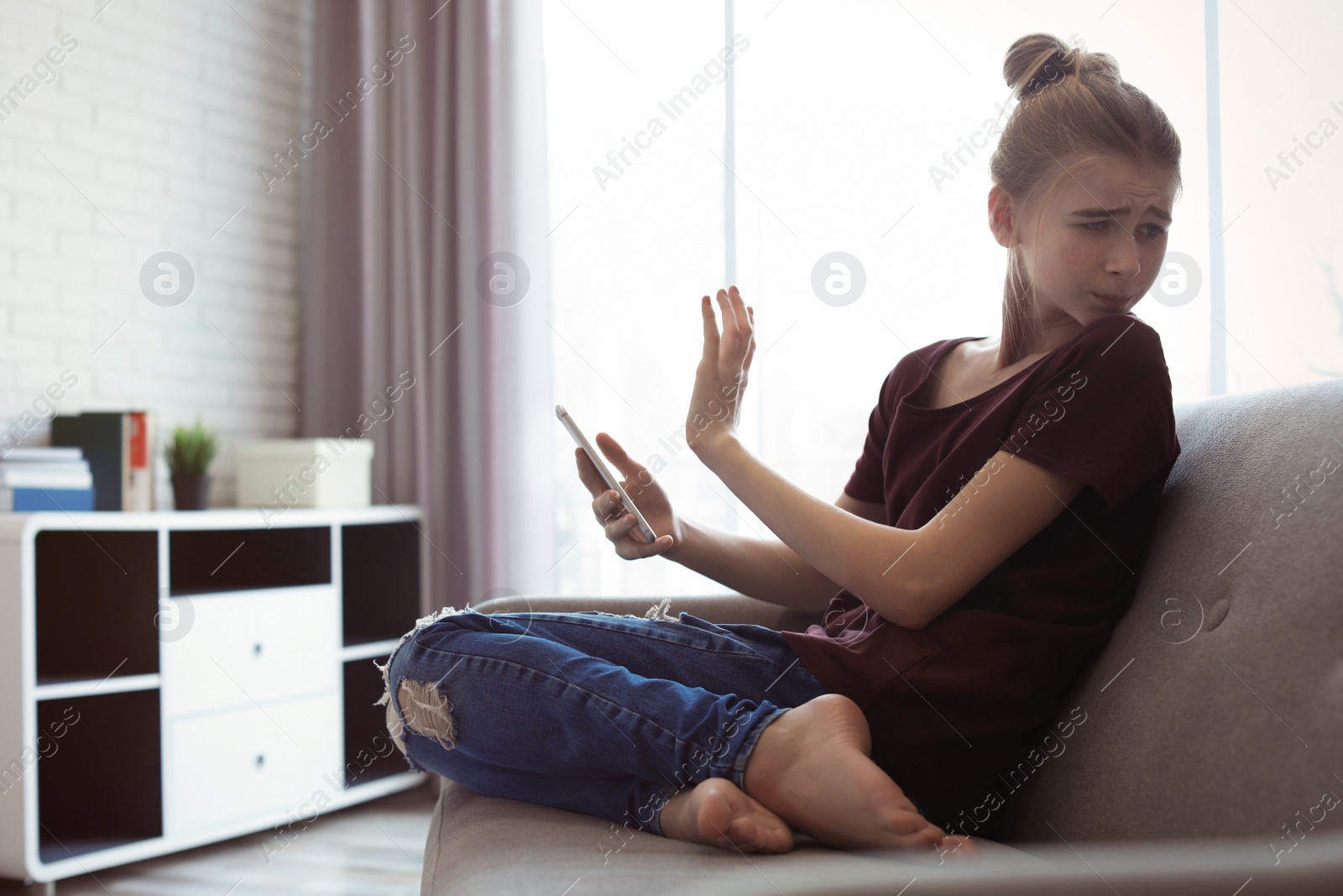 Photo of Terrified teenage girl with smartphone in room. Danger of internet