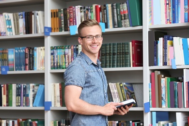 Young man with book near shelving unit in library