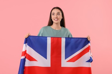 Young woman holding flag of United Kingdom on pink background