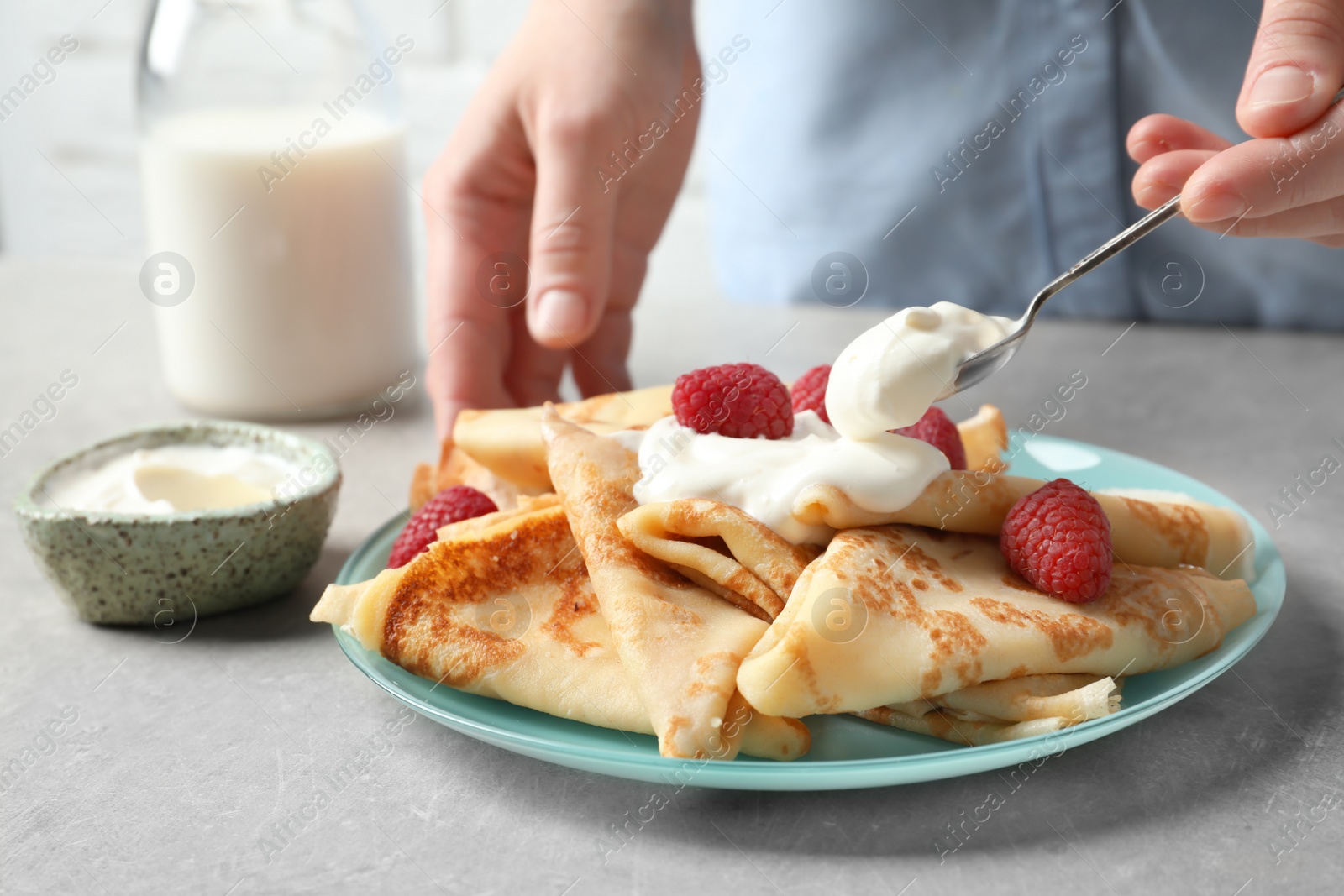 Photo of Woman adding sour cream to thin pancakes with berries at table