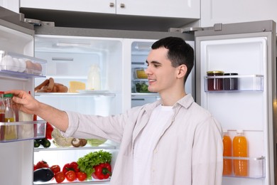 Photo of Happy man taking sauce out of refrigerator in kitchen