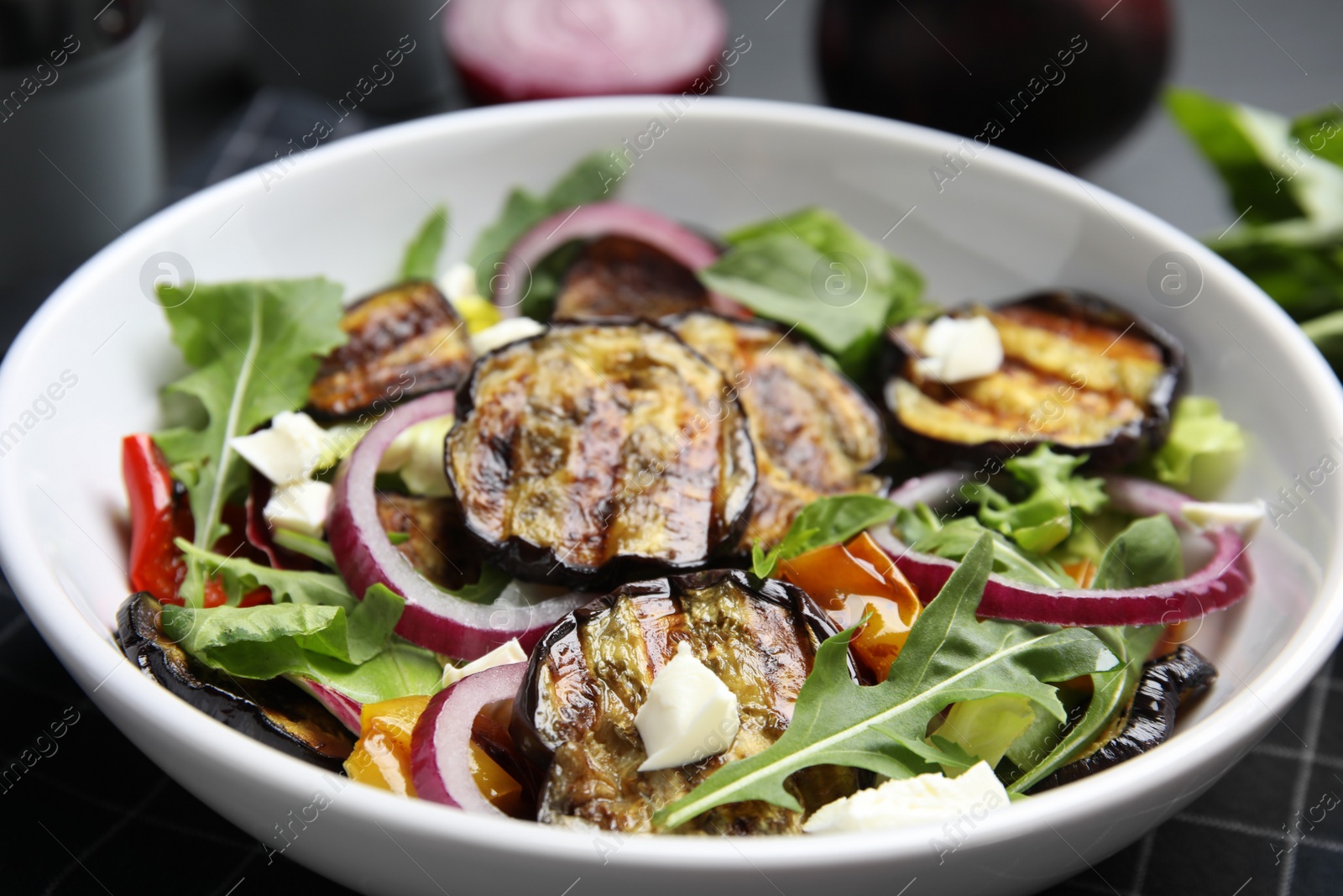 Photo of Delicious salad with roasted eggplant, cheese and arugula in bowl, closeup