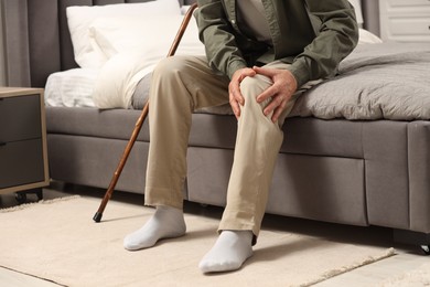 Photo of Senior man with walking cane suffering from knee pain on bed at home, closeup. Rheumatism symptom