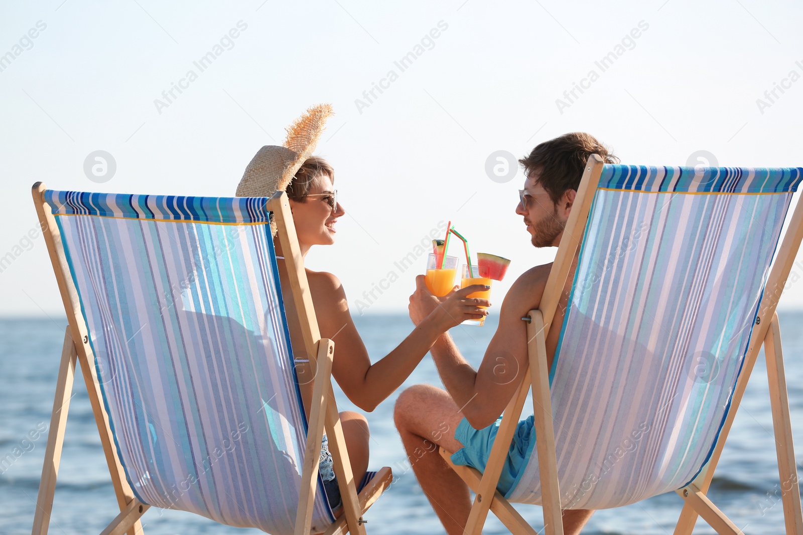 Photo of Young couple with cocktails in beach chairs at seacoast