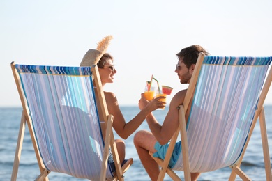 Young couple with cocktails in beach chairs at seacoast