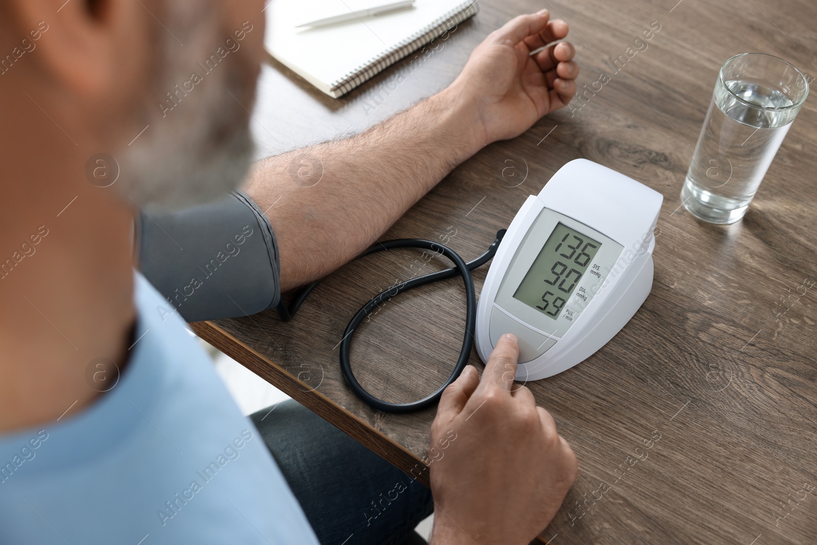 Photo of Man measuring blood pressure at table indoors, closeup