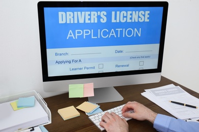 Man using computer to fill driver's license application form at table in office, closeup