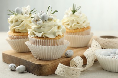 Tasty Easter cupcakes with vanilla cream, candies and ribbon on gray table