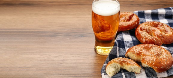 Tasty pretzels and glass of beer on wooden table, space for text. Banner design