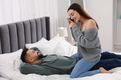 Photo of Happy young couple spending time in bedroom. Smiling woman taking photo of her boyfriend