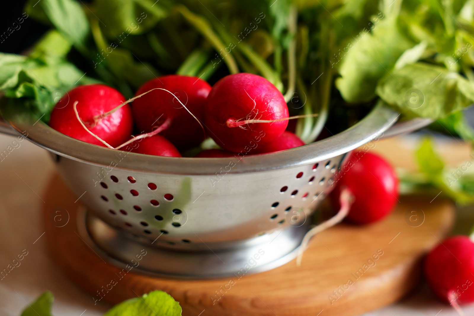 Photo of Metal colander with fresh radishes on white table, closeup