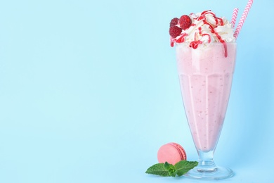 Photo of Tasty raspberry milk shake in glass and macaron on light blue background. Space for text