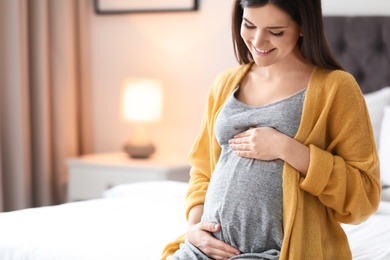 Young pregnant woman sitting on bed at home