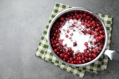 Photo of Making cranberry sauce. Fresh cranberries with sugar in saucepan on gray table, top view. Space for text