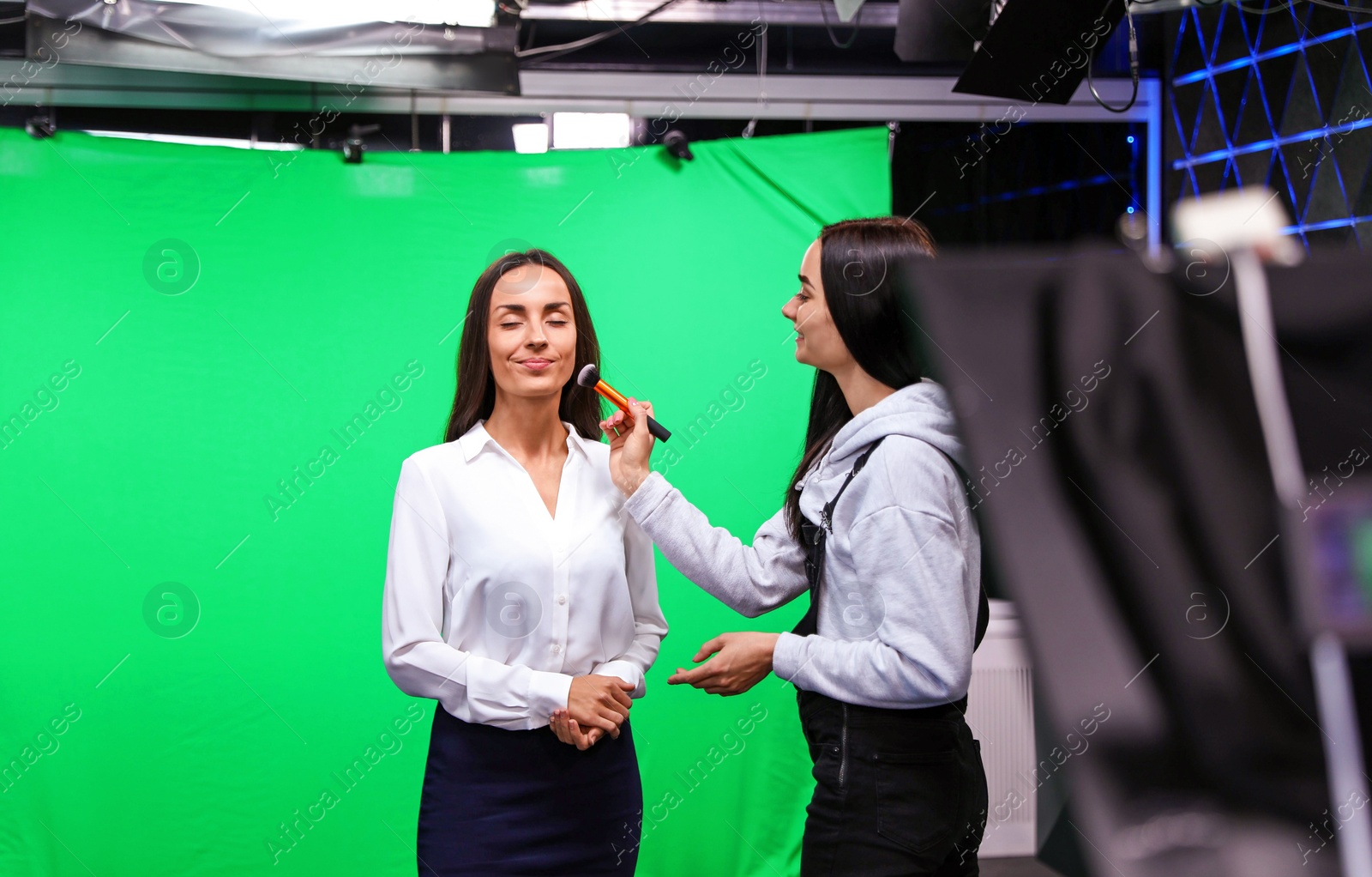 Photo of Presenter, makeup artist and video camera operator working in studio. News broadcasting