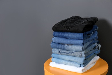 Stack of different jeans on  table against gray background. Space for text