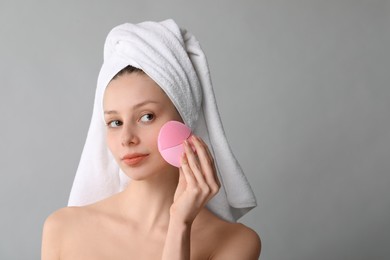 Photo of Washing face. Young woman with cleansing brush on grey background, space for text