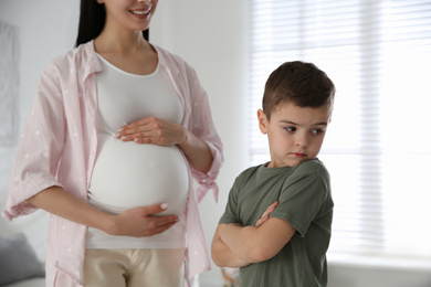 Photo of Unhappy little boy near pregnant mother at home. Feeling jealous towards unborn sibling