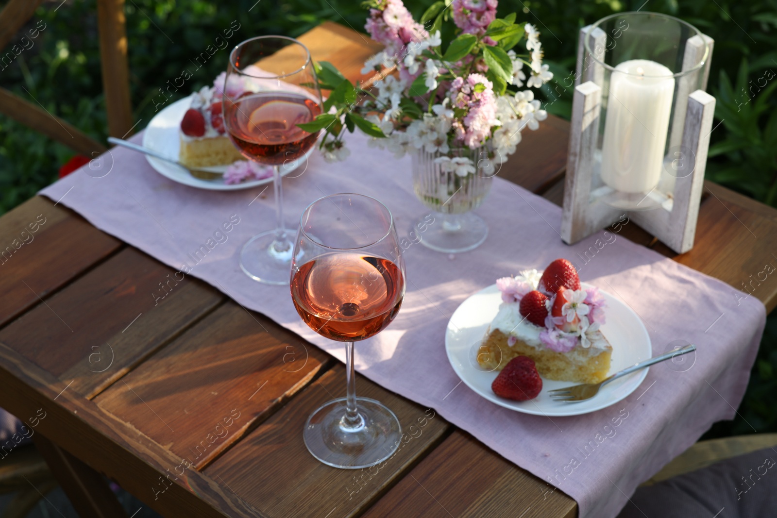 Photo of Vase with spring flowers, wine and cake on table served for romantic date in garden