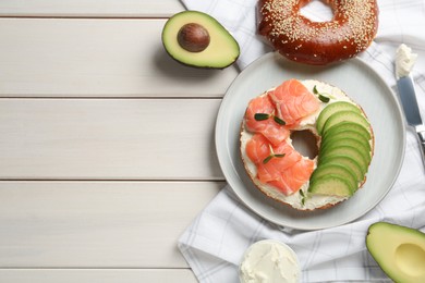 Delicious bagel with cream cheese, salmon and avocado on white wooden table, flat lay. Space for text