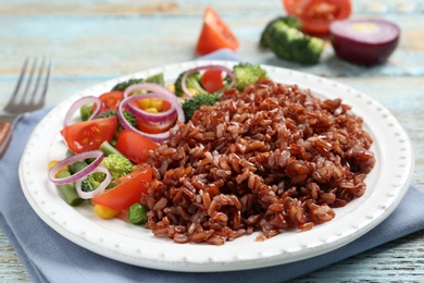 Photo of Plate of cooked brown rice with vegetables on table, closeup