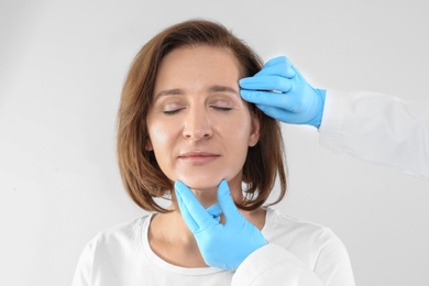 Doctor examining mature woman face before cosmetic surgery on white background